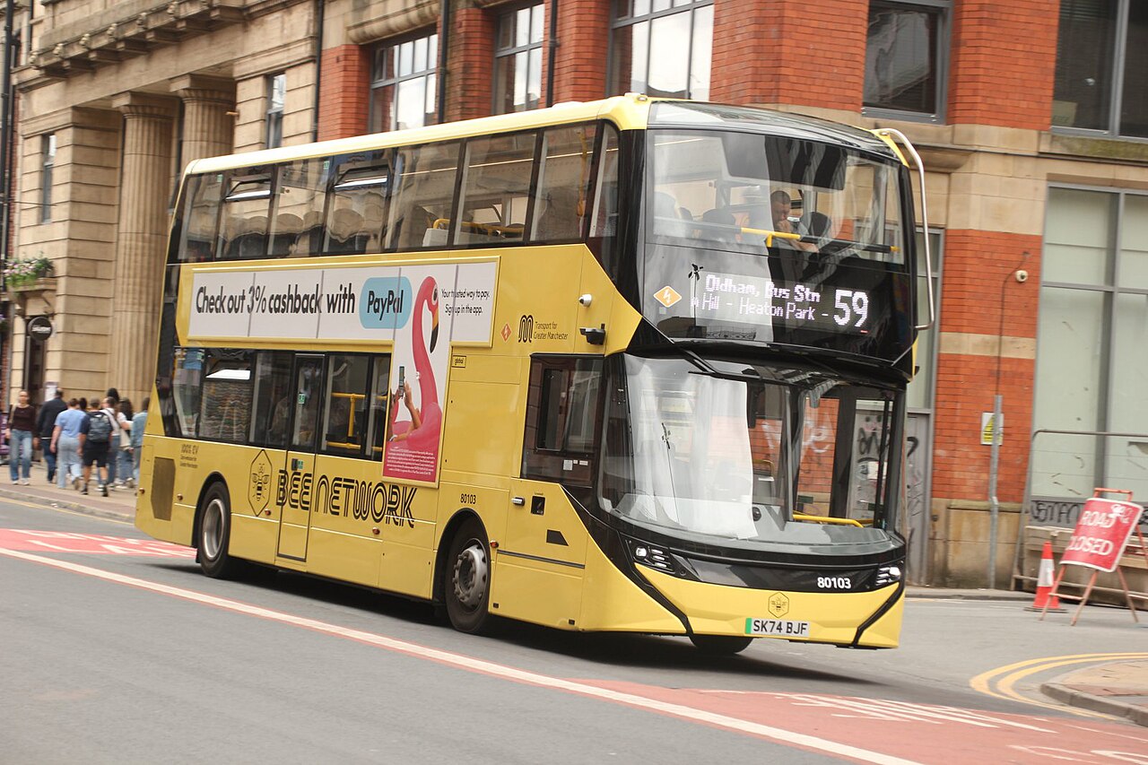 A yellow double-decker Bee Network electric bus travelling through Manchester’s Northern Quarter.